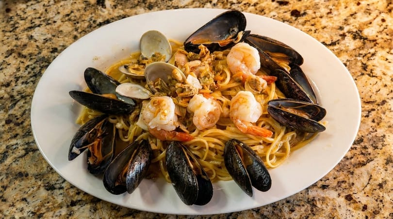 Seafood linguine pasta with mussels, clams, and shrimp on a white plate.