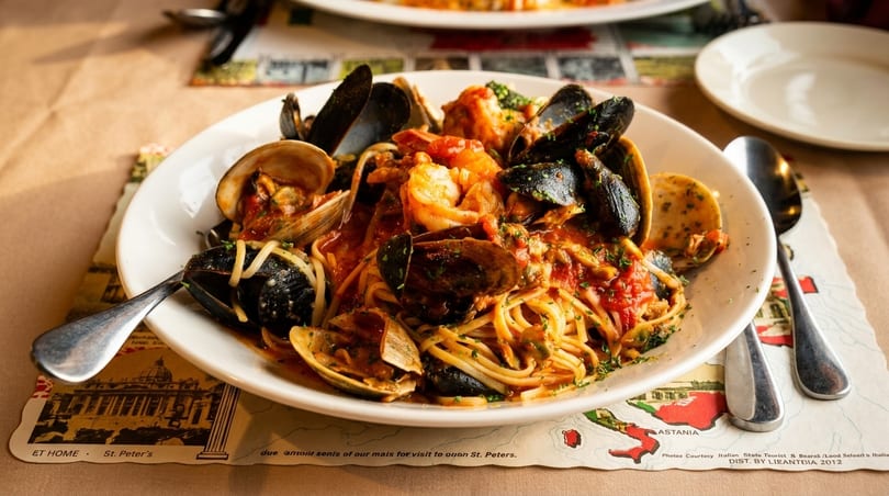 A white bowl of spaghetti with mussels, clams, and shrimp in red sauce on a placemat.