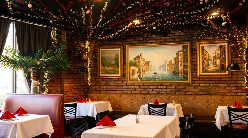 Cozy restaurant interior with brick walls, framed art, red and white floral ceiling decor, and set tables.
