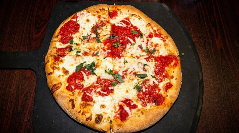 A freshly baked, sliced Margherita pizza with bright red sauce, melted mozzarella, and basil leaves.