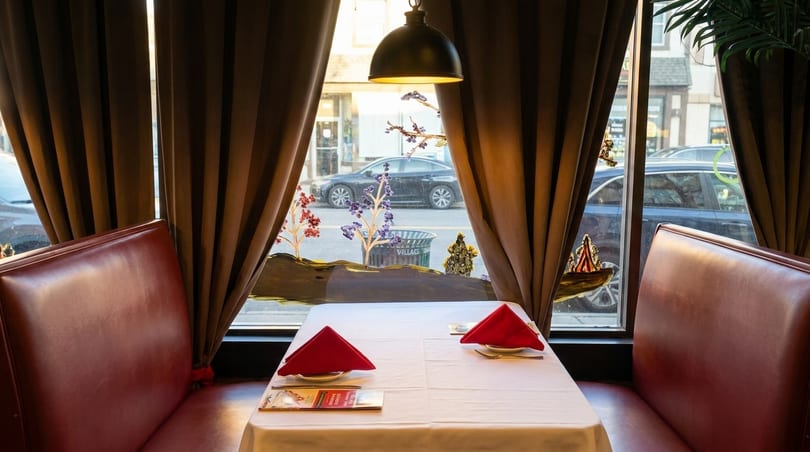 Cozy restaurant booth with red seating, white tablecloth, red napkins, and a street view.