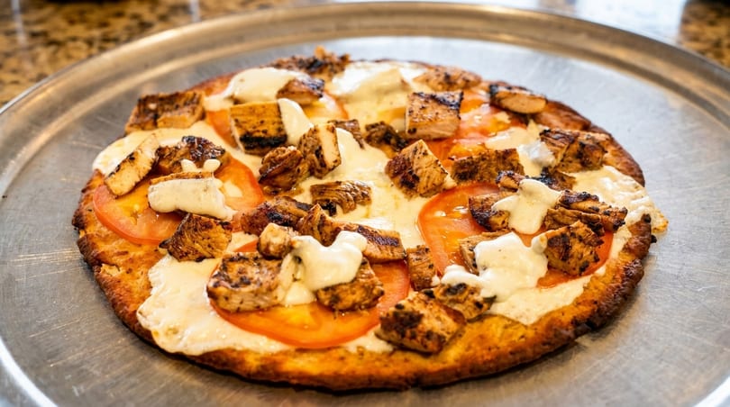 Grilled chicken and tomato pizza with white sauce on a metal tray.