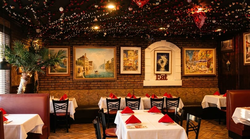 Cozy restaurant interior with brick walls, framed art, red booths, and tables set with white cloths and red napkins.